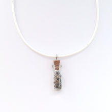 White artistic necklace with a charm that is a small bottle with broken clock pieces in it.